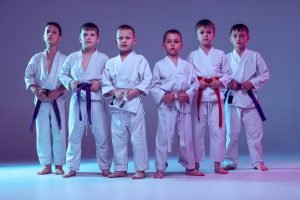 A group of young children dressed in martial arts clothing standing upright. The picture depicts discipline and focus which the children have gained through the training of martial arts. The picture aids with the linking of increased discipline within children to improved creativity and imagination.